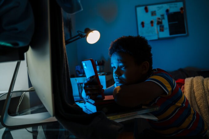 Black boy using mobile phone while sitting by computer screen