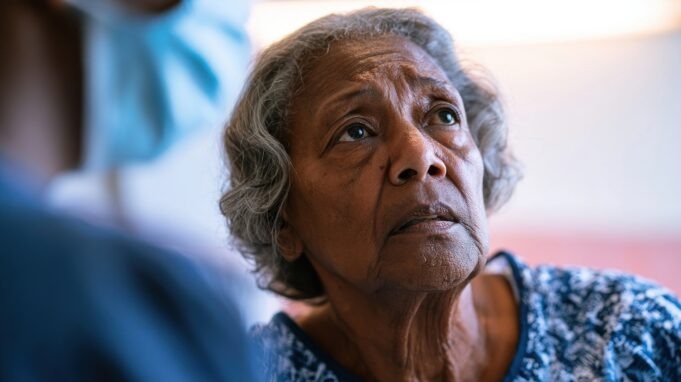 Elderly african american woman looking up with concern at a person in medical scrubs and face mask
