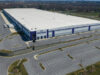 Maryland residents challenge warrantless ICE arrests in federal lawsuit A large industrial warehouse with a white roof and blue accents is surrounded by empty parking lots and roads in a rural area. Description generated by AI