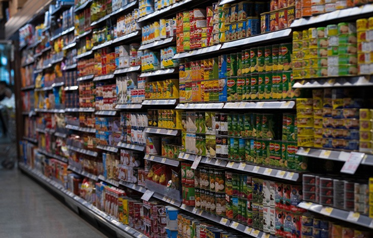 A supermarket aisle filled with shelves stocked with a wide variety of canned and packaged food products. Description generated by AI