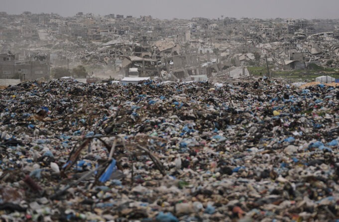 a-vast-expanse-of-garbage-and-debris-stretches-acr A vast expanse of garbage and debris stretches across the foreground with a densely packed area of heavily damaged and ruined buildings in the background under a gray sky. Description generated by AI