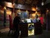 Africa’s mother tongues are finding new life as youth connect with roots and relatives Three adults wearing traditional headwraps are seated around a decorated wooden table in a warmly lit room with patterned walls and a chalkboard menu behind them. Description generated by AI