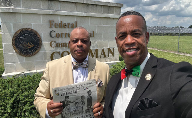 Nation of Islam reestablishes Prison Reform Ministry outreach at Coleman Correctional Complex Two adults dressed in formal attire stand outdoors in front of a sign for a federal correctional complex under a partly cloudy sky. Description generated by AI